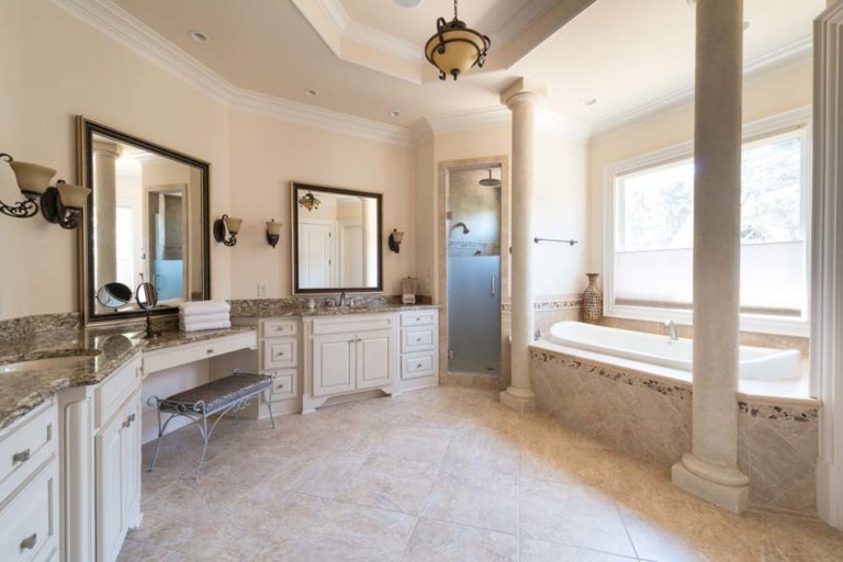 Spacious master bathroom with lots of natural light from large window above tub, which is flanked by two columns.