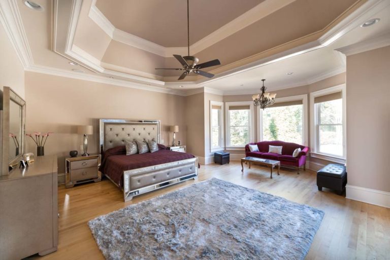 Bedroom with tray ceiling, hardwood floors, and bay windows.